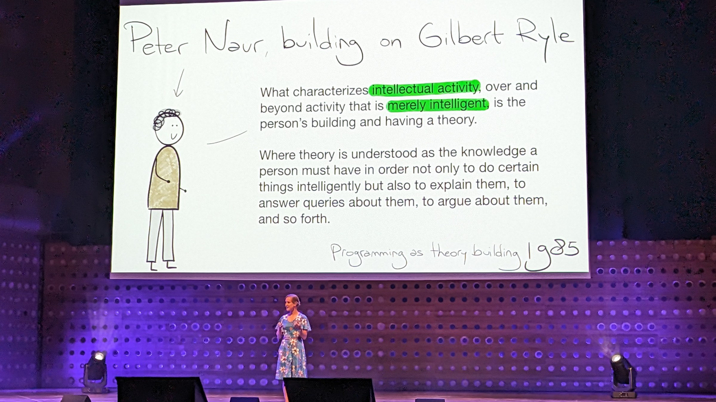Felienne on stage talking. The slides shows excerpt from Peter Naur's paper 'Programming as theory building'
